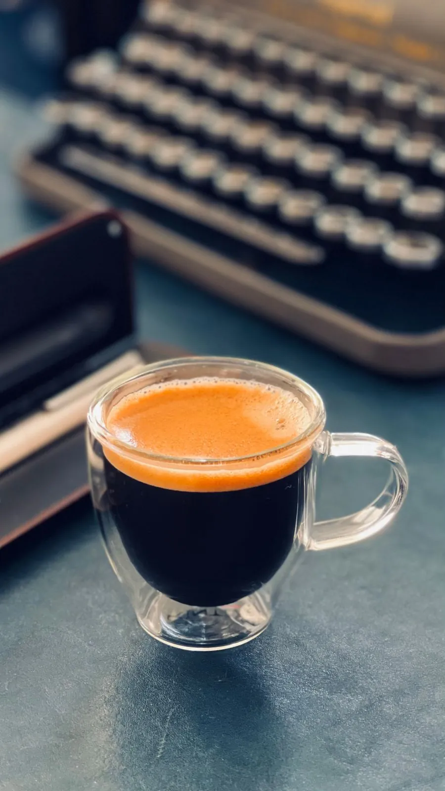 A glowing amber espresso shot in a glass on a dark table